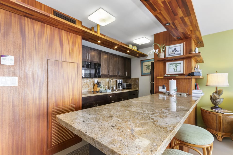 Picture yourself preparing meals on gleaming granite countertops in this tropical-inspired kitchen. Modern appliances and warm wood cabinetry create an inviting space where your vacation culinary adventures begin.