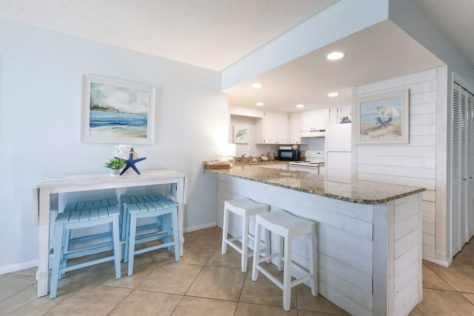 The kitchen features white cabinetry, granite countertops, and cozy breakfast bar with blue stools, perfect for casual dining