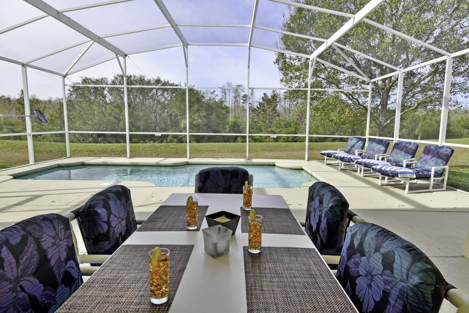 Covered outside dining table with seating for six and screened pool view.