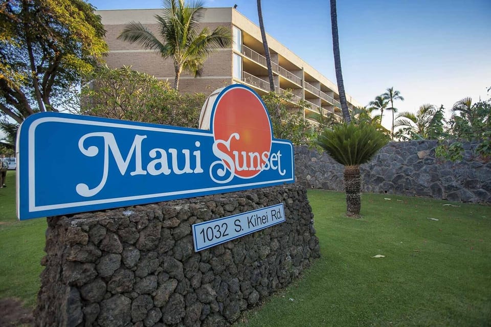 The Maui Sunset property is located at 1032 S. Kihei Rd., welcoming guests with tropical landscaping and a well-maintained entrance surrounded by palm trees and greenery.