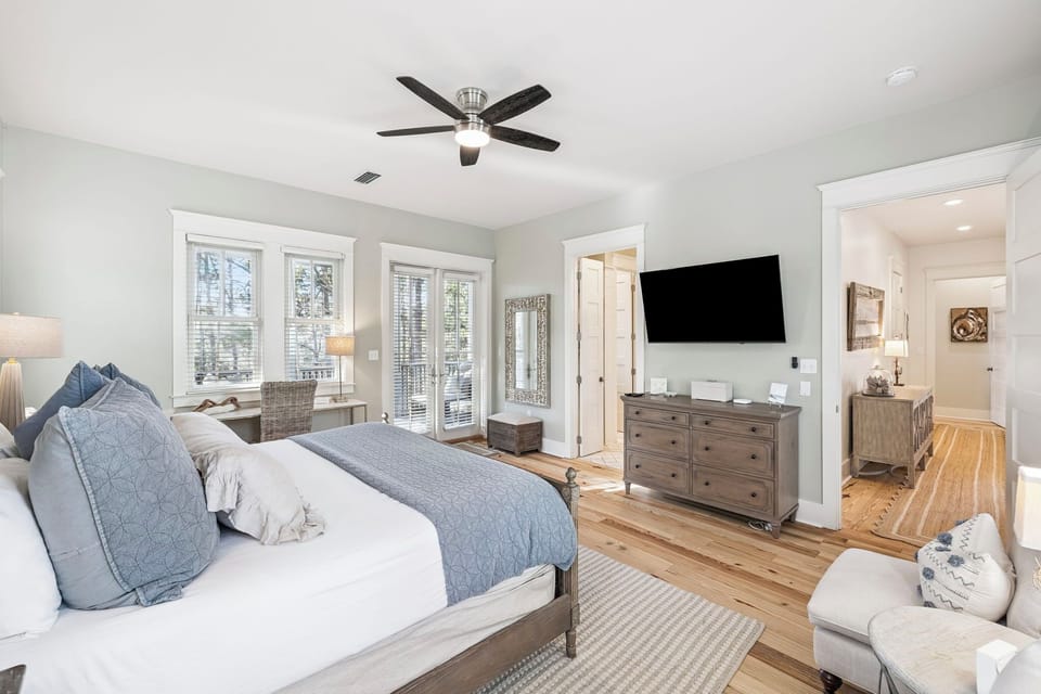 Relax in your serene master suite with plush bedding, ceiling fan, and entertainment center for cozy evenings.