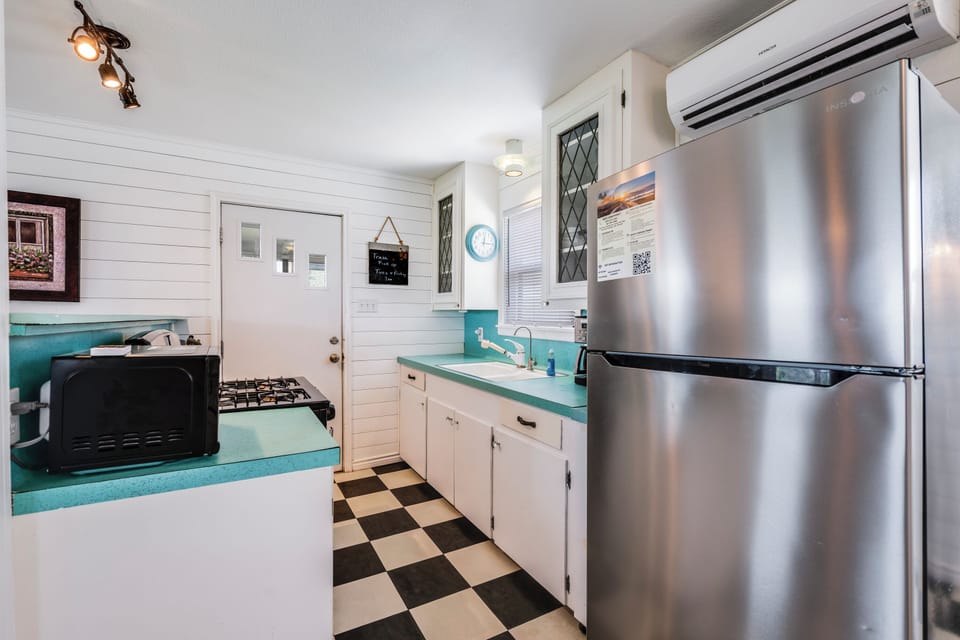 Your charming retro kitchen features everything you need—stainless steel appliances, gas stove, and crisp white cabinetry with turquoise countertops over classic checkered floors.