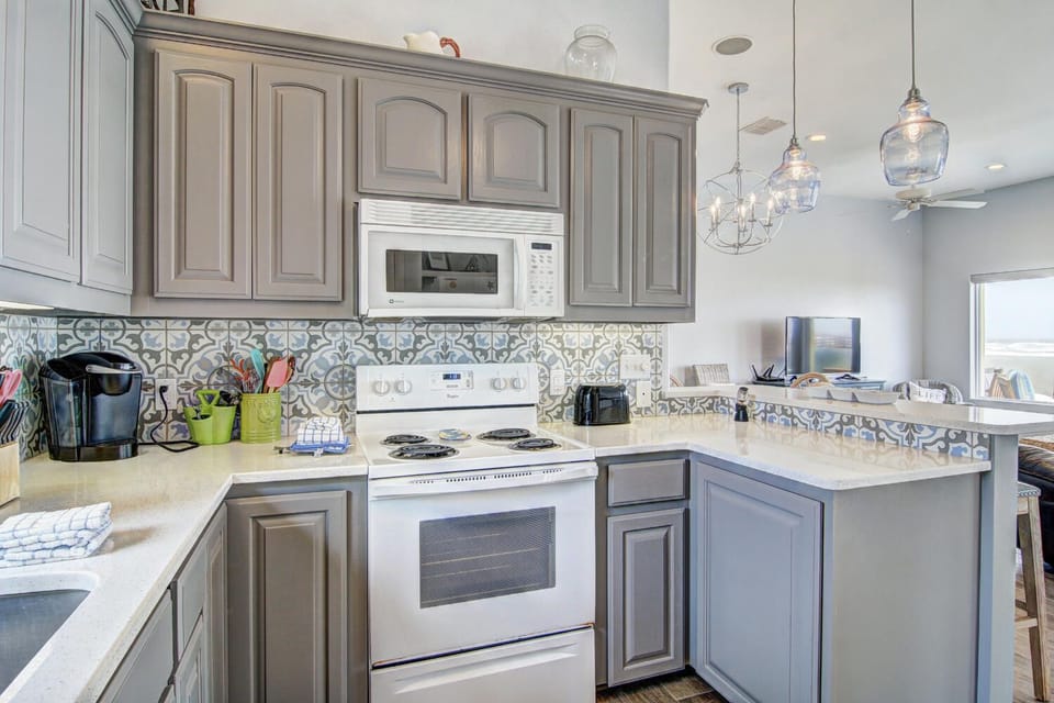 Step into your fully equipped kitchen where elegant gray cabinets and stylish pendant lights create the perfect space for cooking.