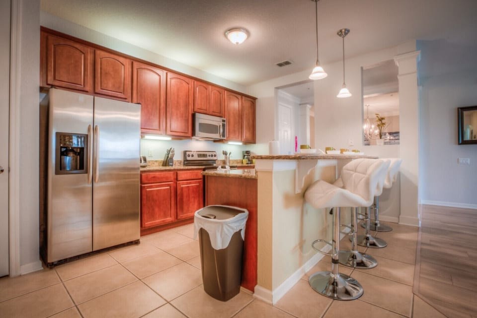 Indulge in our warm-colored kitchen of the condo in Orlando - Complete with a convenient counter table with high chairs - Elegant lighting throughout the space - Plenty of storage space - Fully equipped with all kitchen accessories