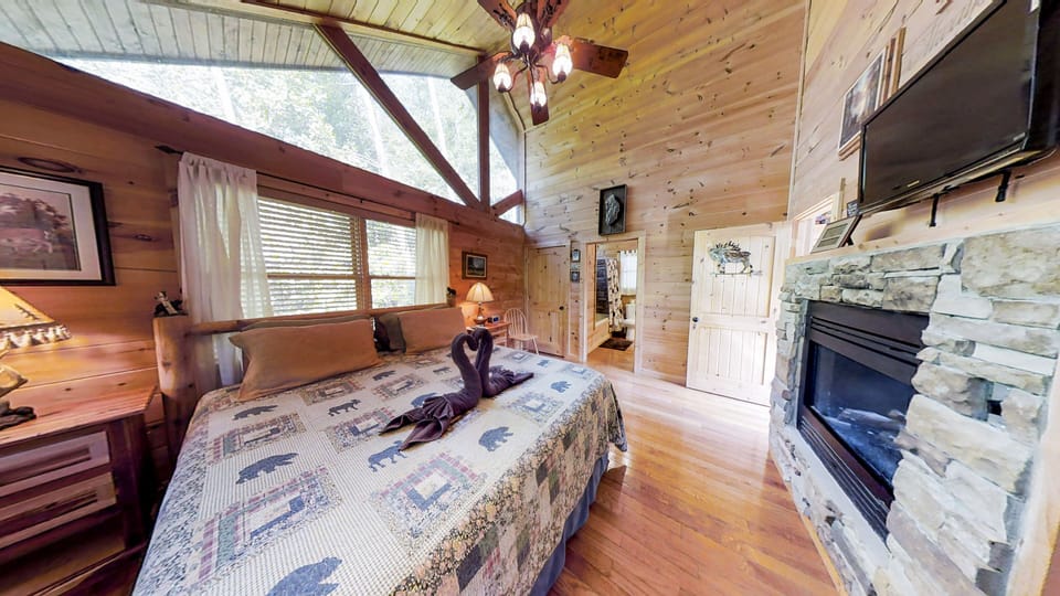 Cozy king bedroom with a two-sided gas fireplace, rocking chair, and warm wood cabin walls at Always Kiss Me Goodnight cabin in Pigeon Forge, Tennessee — just 10 minutes from downtown Pigeon Forge.