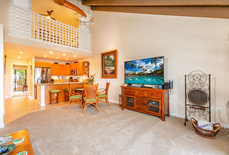 Step into your open-concept haven where vaulted ceilings and warm Hawaiian décor welcome you. Unwind in the living area with tropical artwork, then gather around the dining table or kitchen—all bathed in natural light and island charm.
