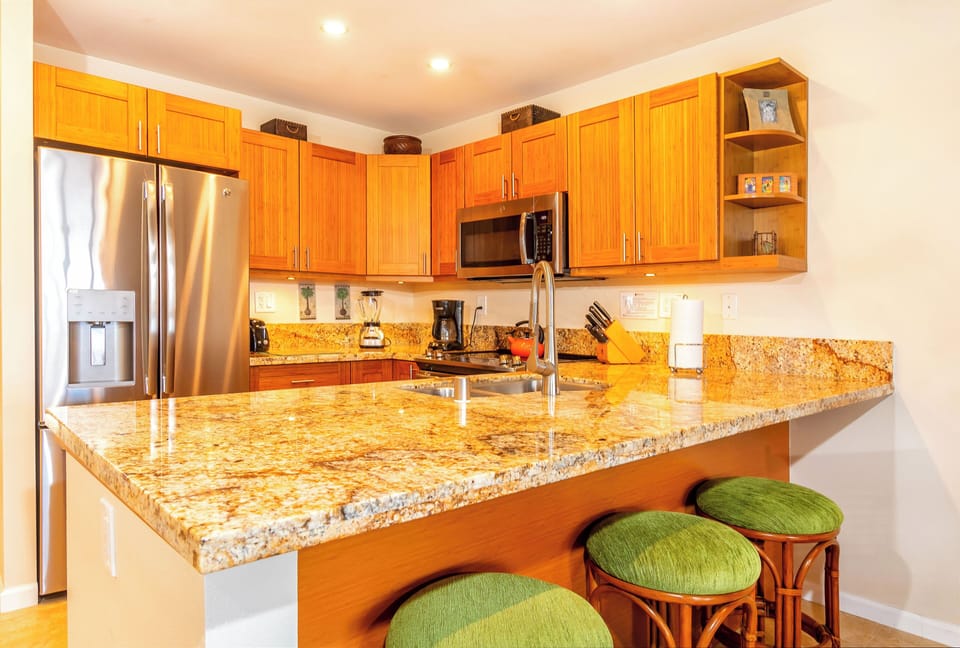 You'll love preparing meals in this bright, fully equipped kitchen featuring granite countertops, stainless steel appliances, and a handy breakfast bar with tropical-style seating—perfect for your morning coffee.