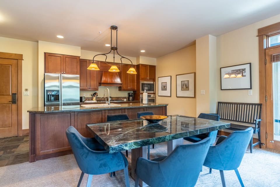 Gather around this stunning granite dining table in your open-concept space, where rich wood cabinetry and modern appliances create the perfect backdrop for memorable meals together.
