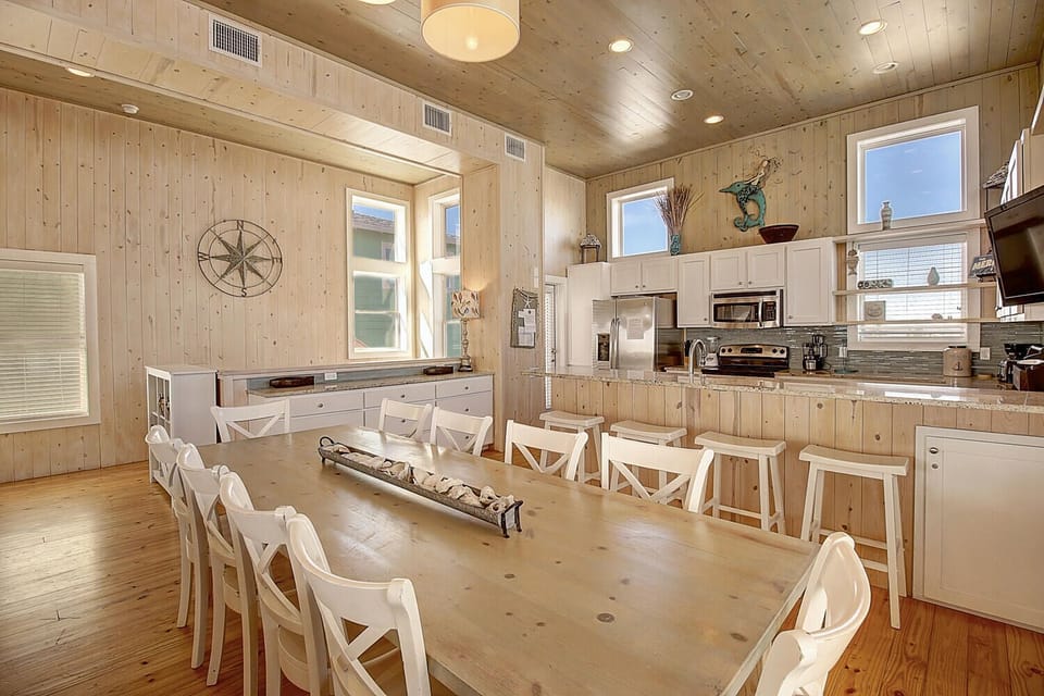 Your coastal dining space features warm wood walls, stainless appliances, and seating for ten around the inviting farmhouse table.