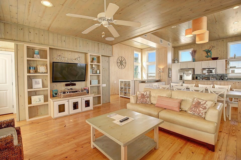 Relax in your cozy living space with warm wood walls, plush seating, and entertainment center—perfect for unwinding after beach days.