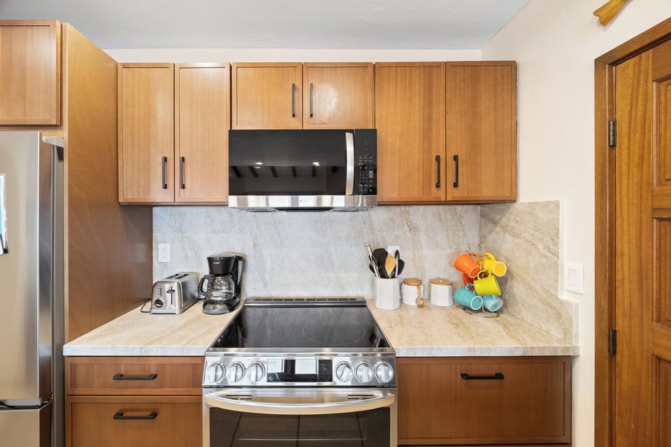 Your fully equipped kitchen features warm wood cabinetry, modern appliances, and countertops with elegant marble backsplash—perfectly set up for preparing meals with ease and comfort during your stay.