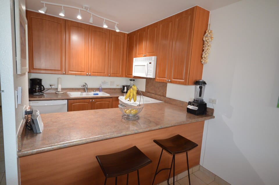 Your fully equipped kitchen awaits with rich wood cabinetry, modern appliances, and a breakfast bar—perfect for preparing tropical meals and enjoying morning coffee together.