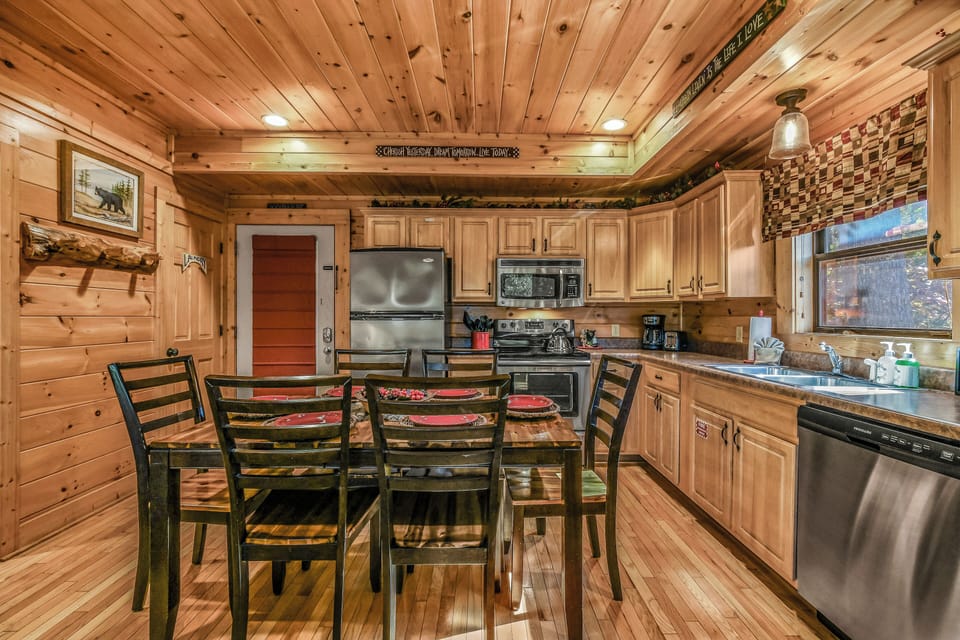 Kitchen with full size stainless refrigerator, stove, microwave, and adjacent dining table at A Stairway to Heaven cabin in Wears Valley, Tennessee