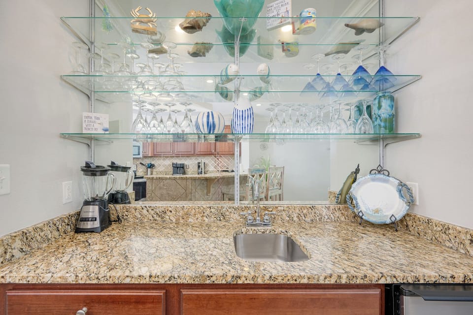 A stylish wet bar features granite countertops, glassware display, and modern appliances for a delightful experience