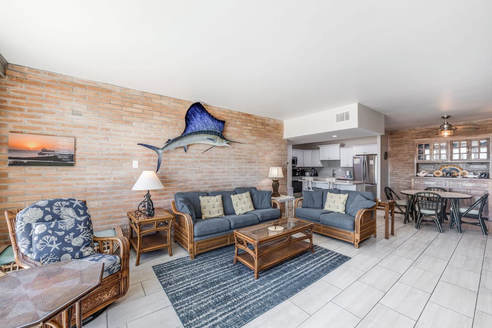 Relax in your coastal-themed living space with nautical touches and bamboo furniture, seamlessly flowing into the open kitchen.