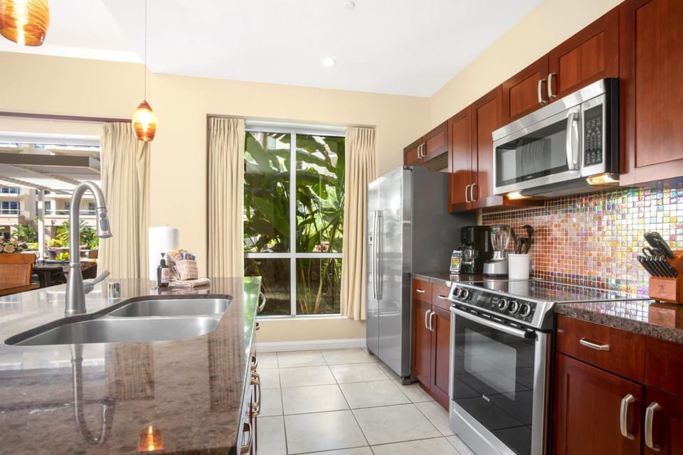 Bright kitchen with window garden views, granite countertops, and built-in stainless steel cooking appliances