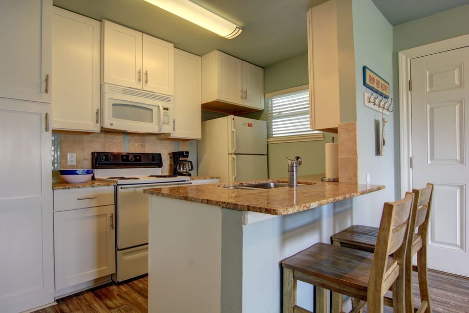 Cook your favorite meals in this bright, fully-equipped kitchen featuring granite countertops, white appliances, and a breakfast bar.