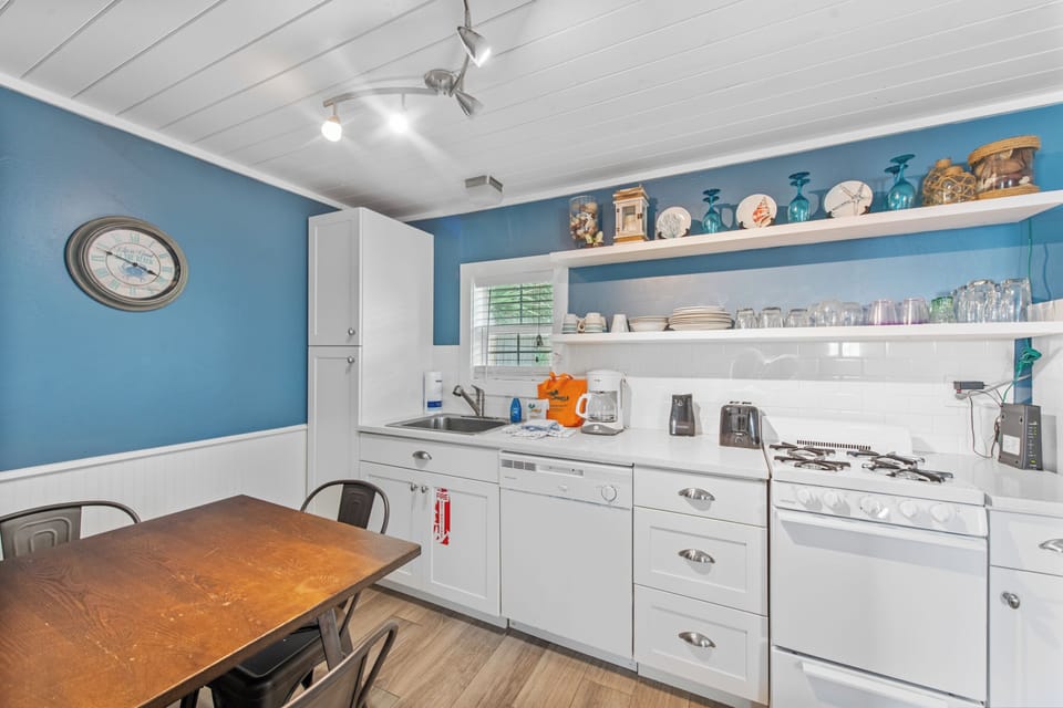 Your charming coastal kitchen awaits with cheerful blue walls, open shelving filled with beach treasures, and everything you need to prepare memorable meals together.