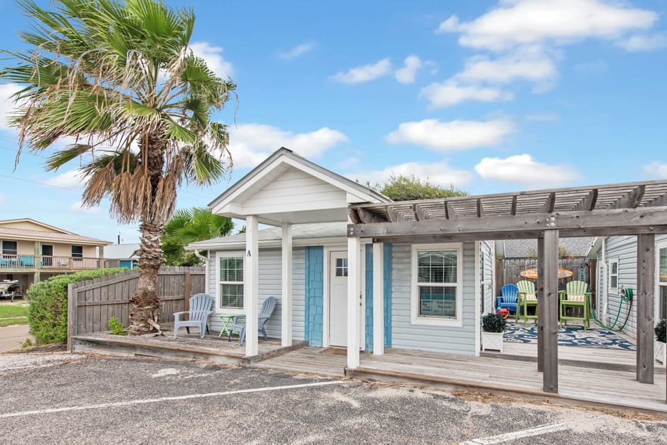 Charming coastal cottage with bright turquoise accents and covered porch area, surrounded by swaying palm trees.