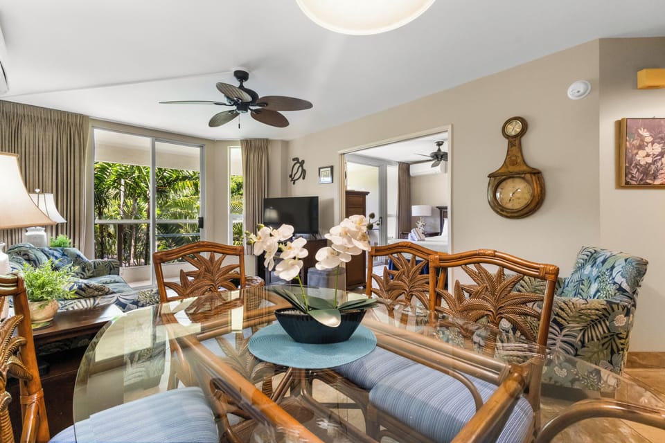 Relax in your tropical-themed dining space with elegant glass table, palm-patterned chairs, and garden views through sliding doors.