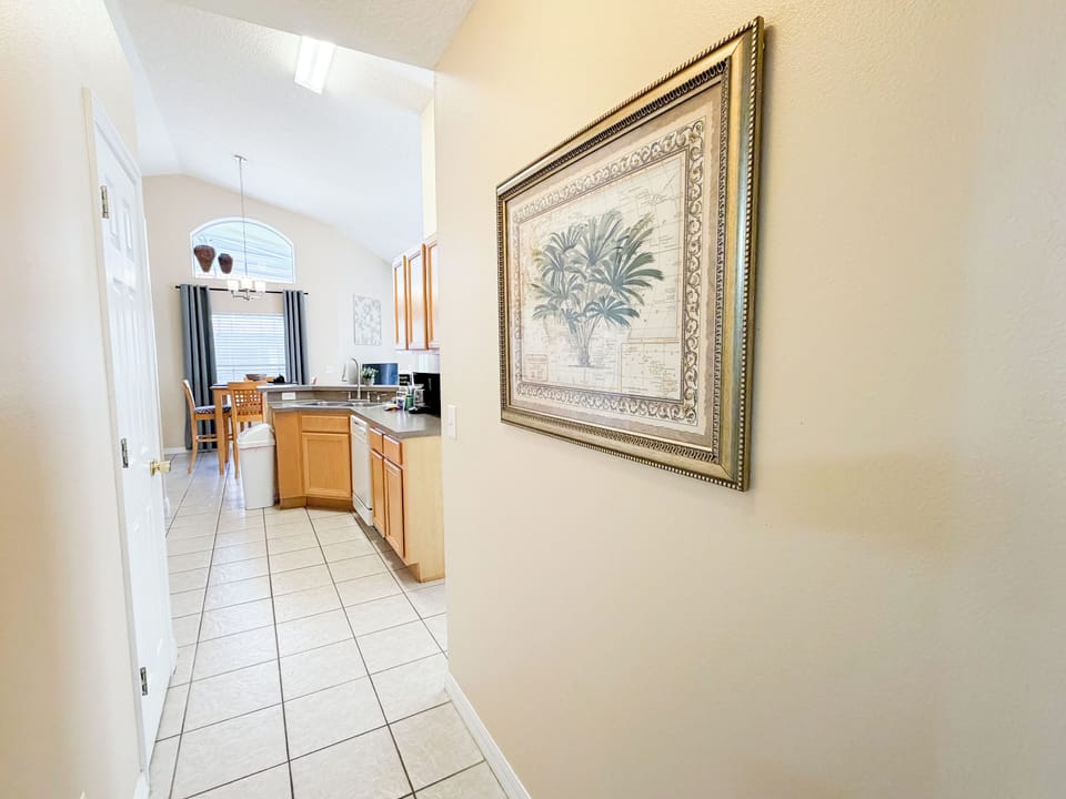 Bright hallway leading into the fully equipped kitchen and dining area, featuring tiled floors, warm cabinetry, and an open, welcoming layout.