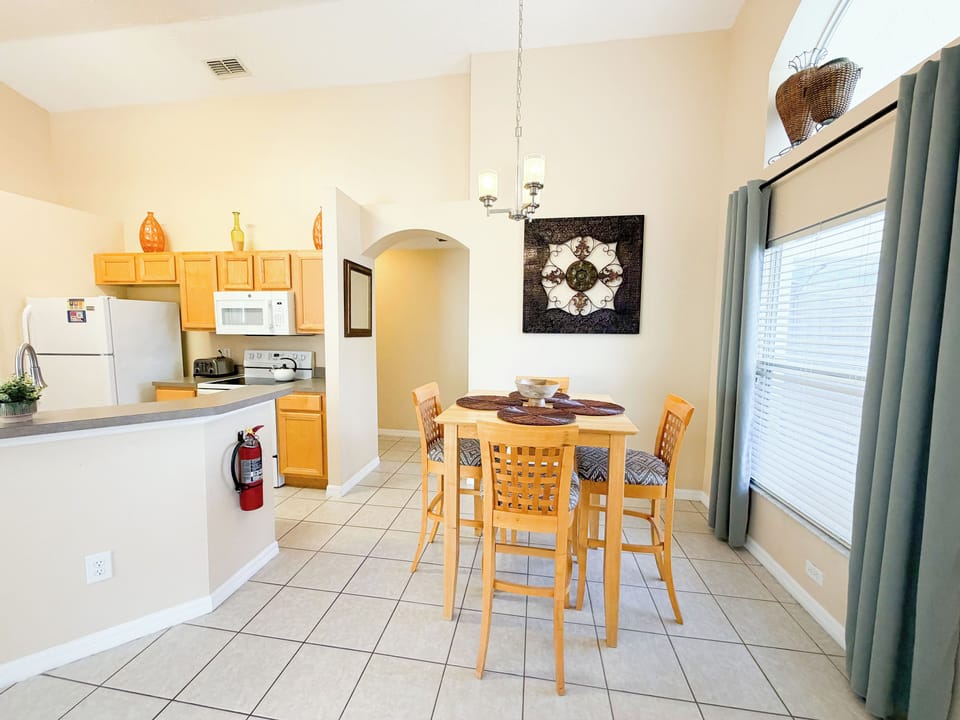 Open kitchen and dining area featuring a breakfast bar, full kitchen appliances, and a dining table for four, with natural light and an open layout ideal for family meals.