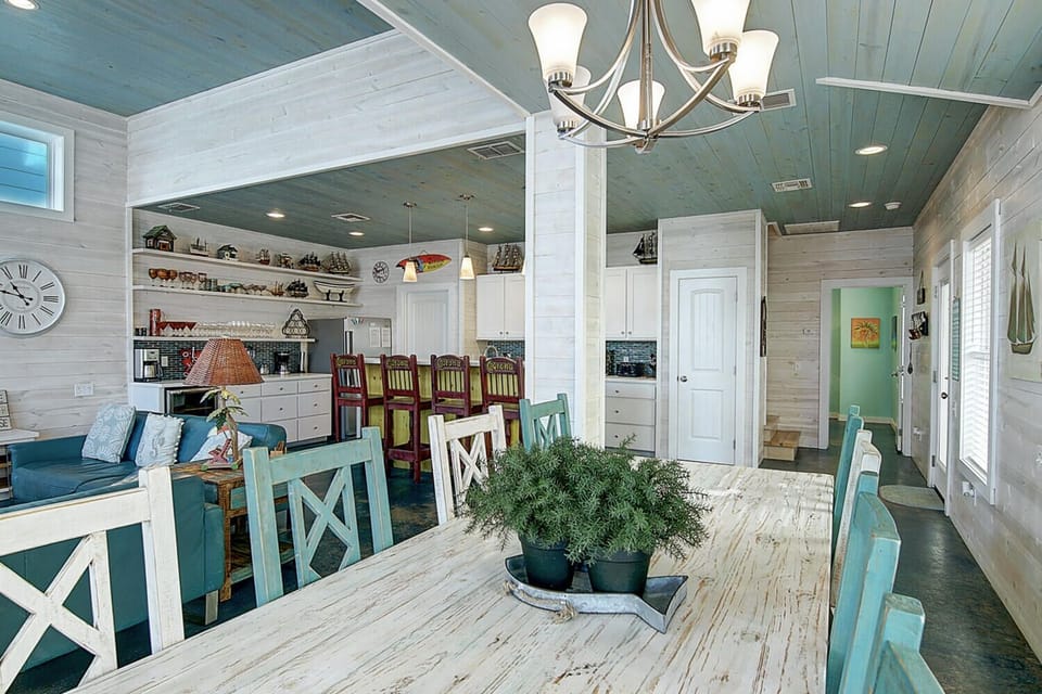 Gather around your rustic farmhouse table beneath coastal-blue ceilings where warm chandeliers cast gentle light over shared meals and memories.