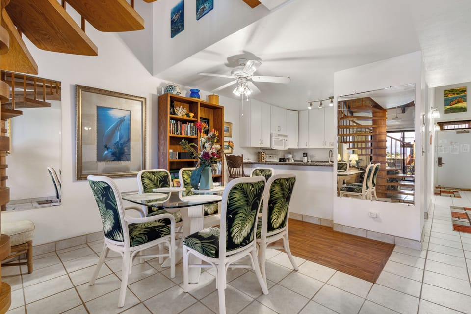Gather around a welcoming dining table where coastal charm meets home comfort. Tropical-print chairs, warm wood shelving, and open kitchen flow create your perfect space for memorable meals and conversation.