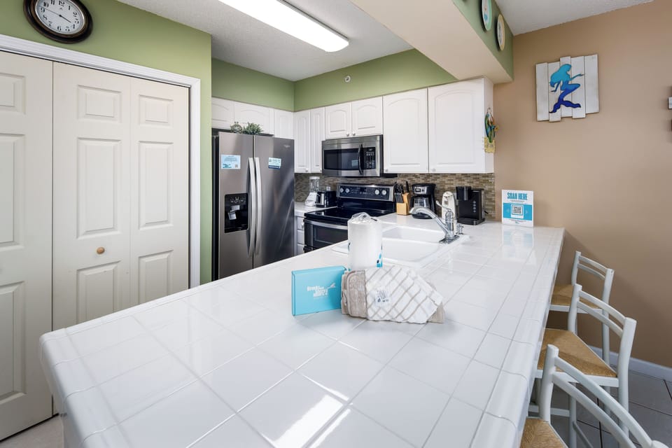 Kitchen - The kitchen of this one-bedroom unit has several nice features, including tiled countertops, Mr. Coffee and Keurig coffee makers and two-sided sink with pull out sprayer. 3 chairs at the island provide additional seating
