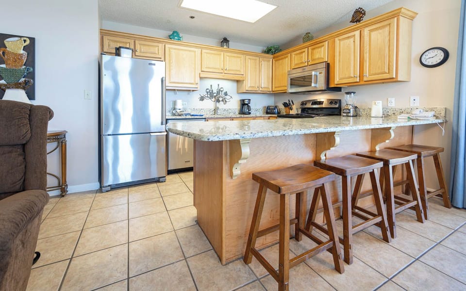 Bright wood cabinetry complements the modern kitchen with a breakfast bar, featuring granite countertops and seating for four