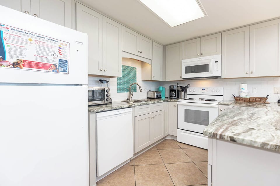 Bright kitchen features sleek cabinetry, a breakfast bar, and white appliances, creating an inviting space