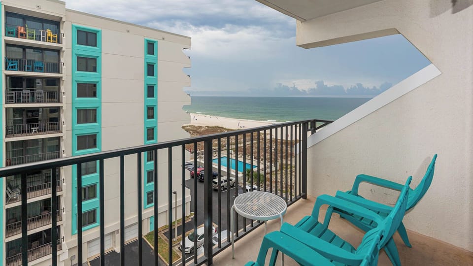 Enjoy a relaxing view of the beach from the balcony, featuring turquoise chairs and a small table for outdoor comfort