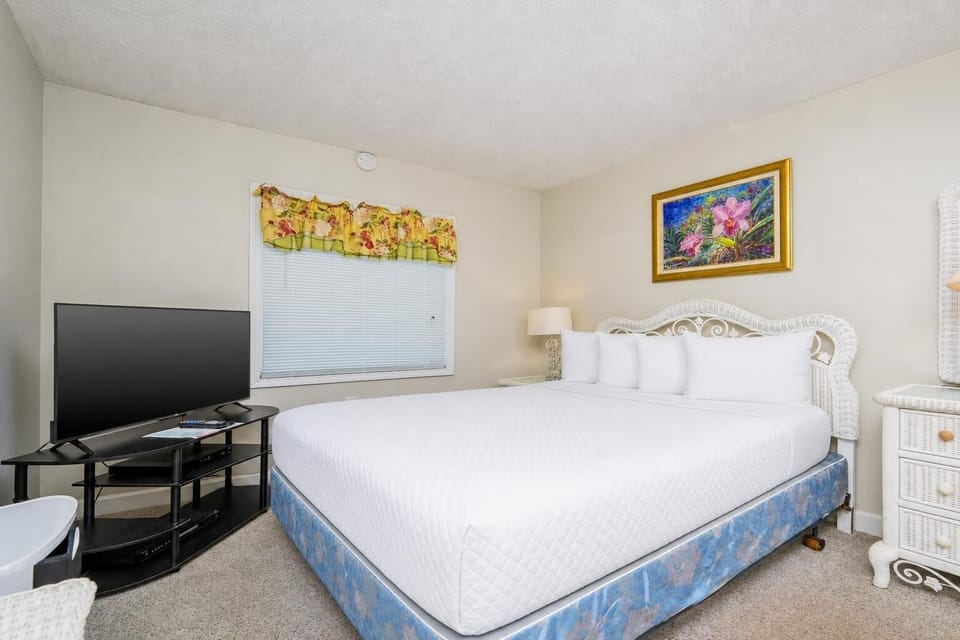 This bedroom features a large bed, a TV for entertainment, and bright floral curtains adding a cheerful touch