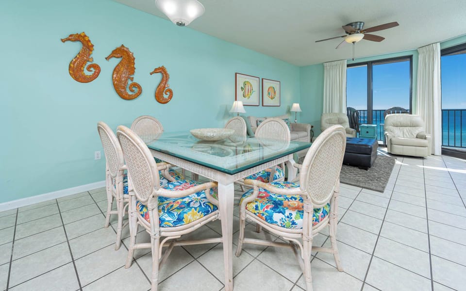Gather around the glass dining table with colorful seating, enjoying the beach views through the balcony doors