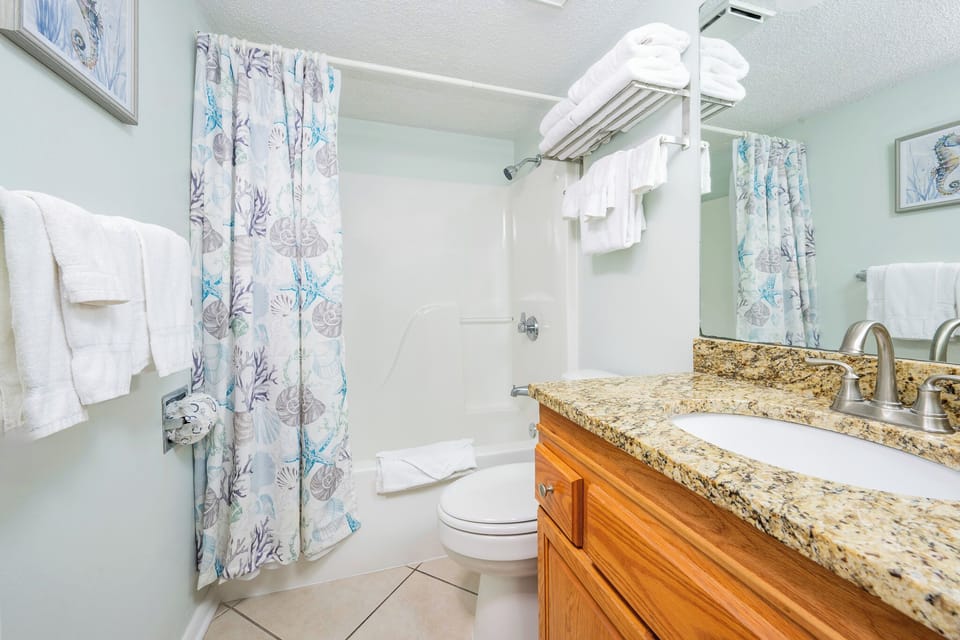 Bright guest bathroom featuring a granite countertop, decorative shower curtain, and fresh towels for a refreshing experience