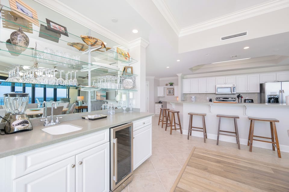 Glassware sparkles above your wet bar where you mix cool drinks and share stories before beach time
