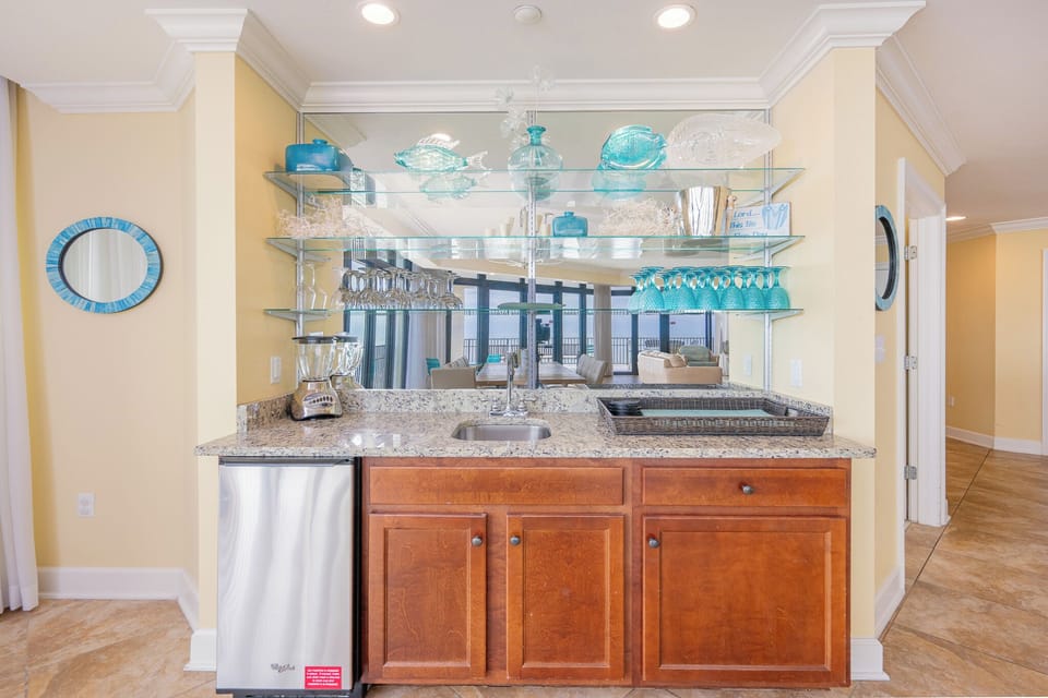 Wet bar area featuring a sleek granite countertop, stainless appliances, and decorative glassware