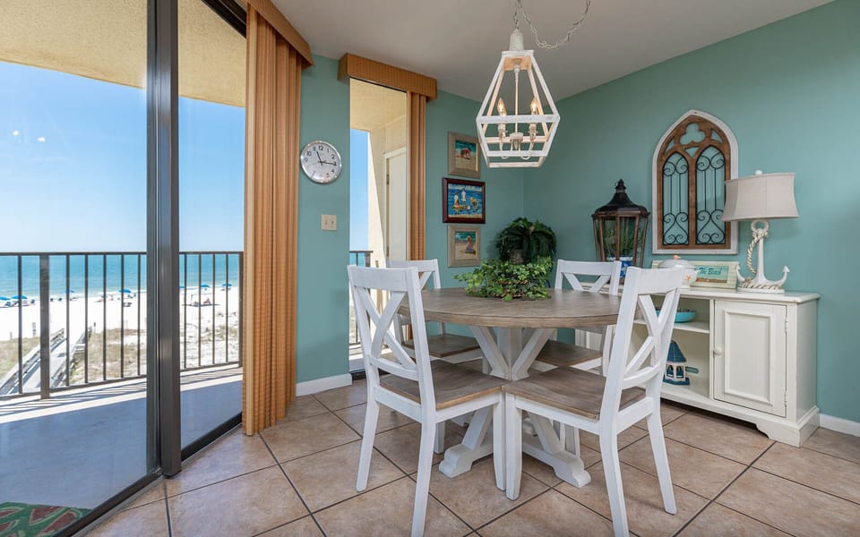 Dining area with a round table, white chairs, and a stunning beachfront view through large glass doors