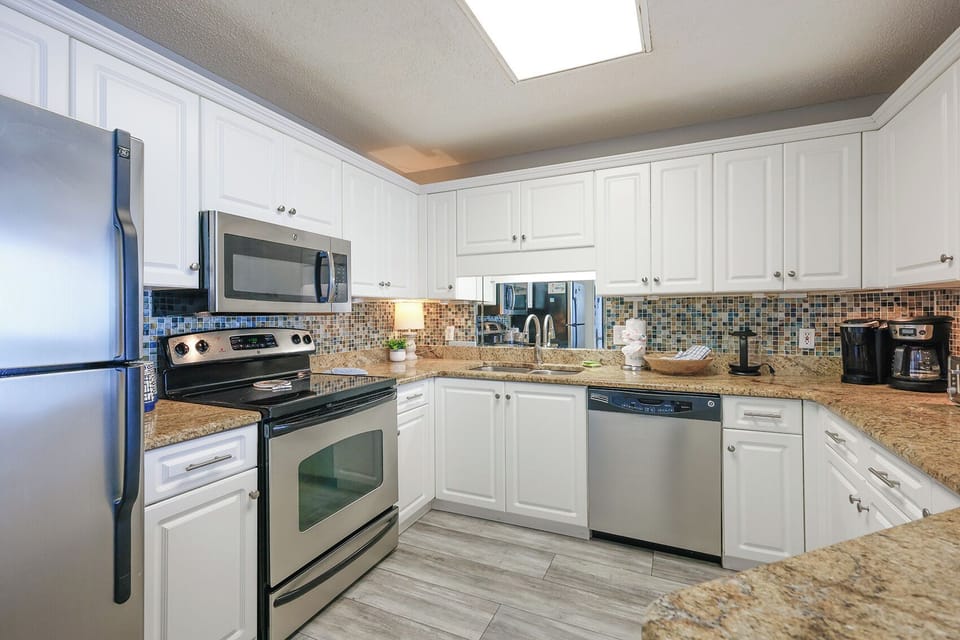 Kitchen featuring white cabinetry, granite countertops, stainless appliances, mosaic backsplash, with a Keurig coffee station