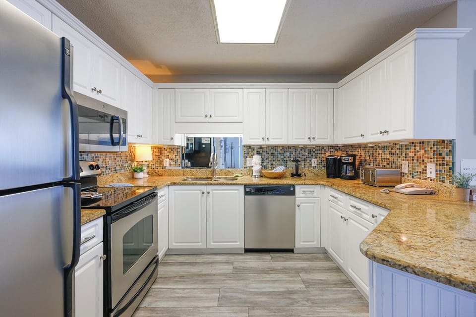 Bright white cabinetry and granite countertops complement the modern kitchen, featuring a breakfast bar and tile backsplash