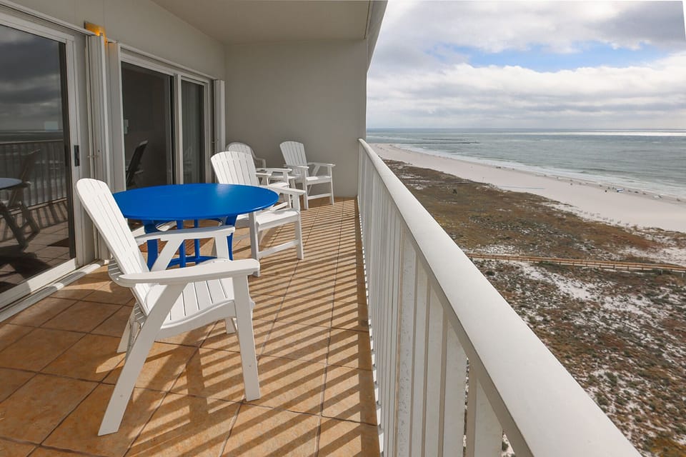 Enjoy a relaxing moment on the balcony with a blue table and white chairs, overlooking the beautiful beachfront view