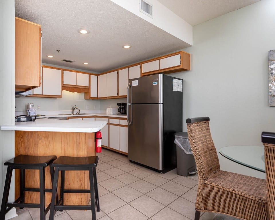 Brightly lit kitchen features wood cabinetry, stainless appliances, and a breakfast bar with seating for casual dining