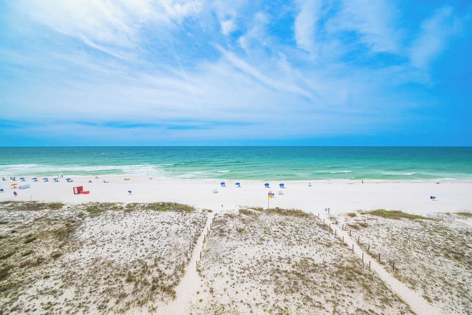 This stunning beachfront view showcases soft white sand and inviting blue waters, perfect for a relaxing getaway