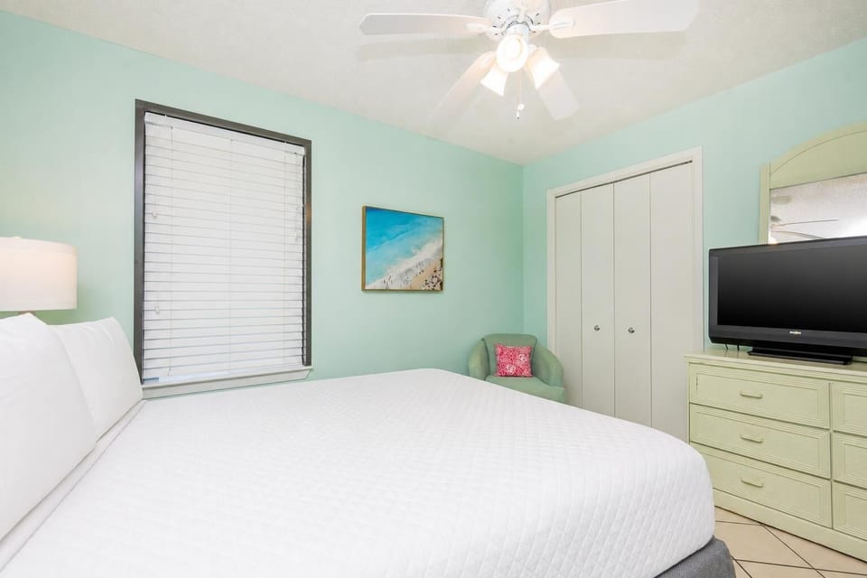 Rest in this cheerful guest bedroom featuring a queen bed, soft decor, a TV, and a cozy chair for relaxation