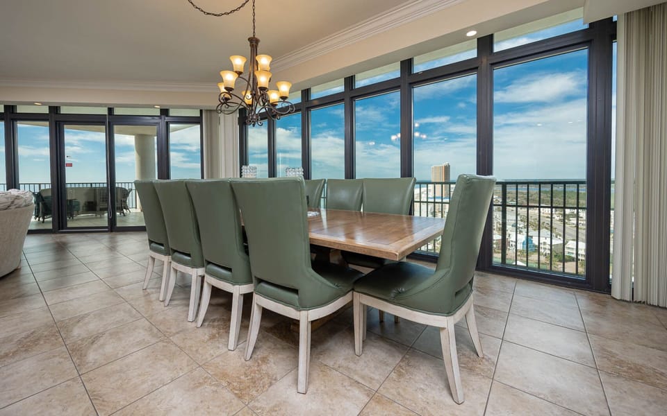 This dining area features a large wooden table surrounded by ten chairs, offering stunning views through expansive windows