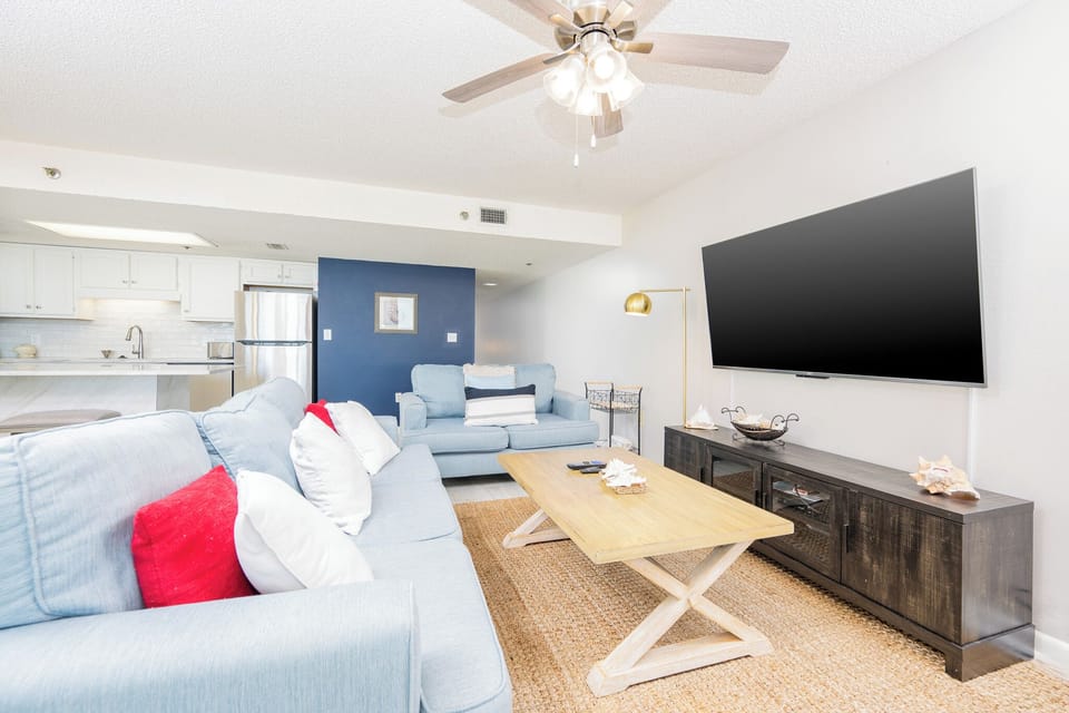 Living area featuring a light blue sofa with queen sleeper, a wooden coffee table, and a large flat-screen TV