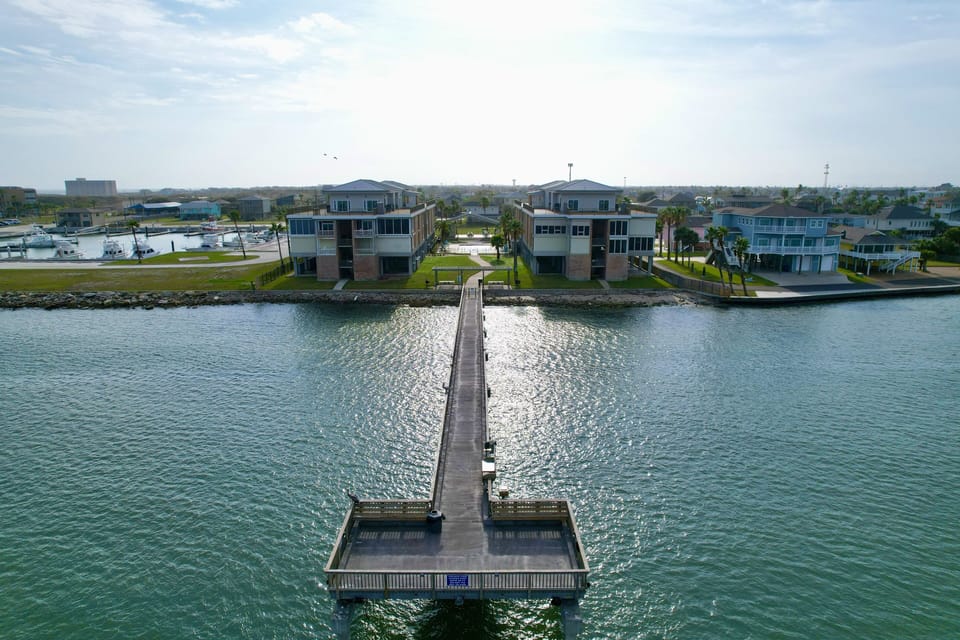 Aerial view of waterfront rental properties connected by a private fishing pier extending into calm turquoise waters.