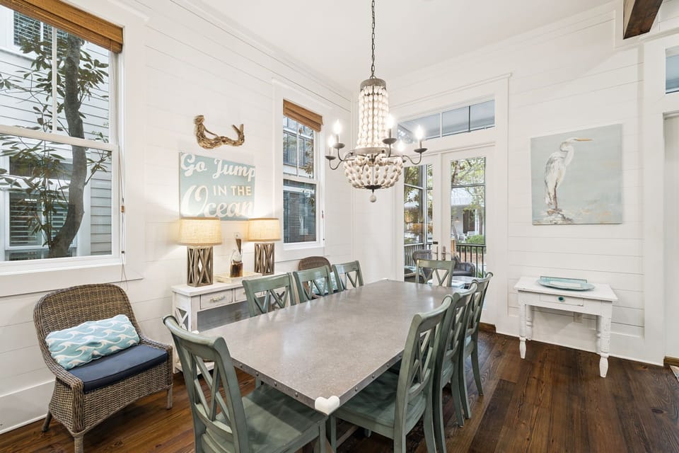 Your bright dining room features coastal charm with sea-green chairs, elegant chandelier, and cheerful ocean-themed decor for memorable meals.