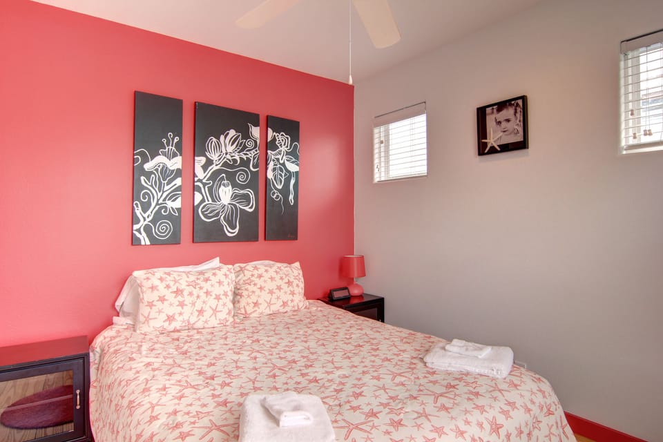 Relax in your cheerful bedroom featuring a vibrant coral accent wall and stylish botanical artwork above your comfortable bed.