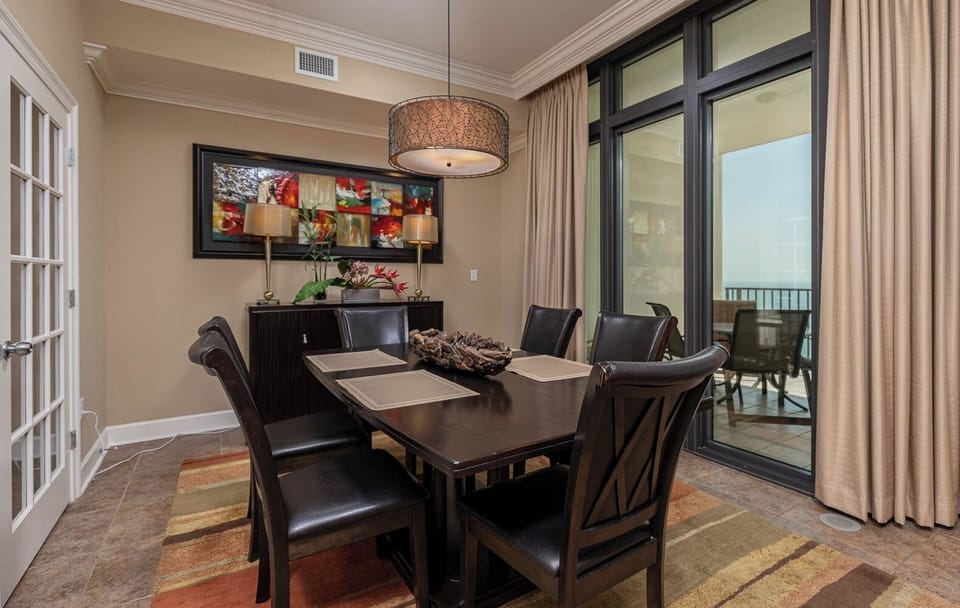 This dining area features a stylish table with dark chairs, vibrant artwork, and a view of the beach through large windows